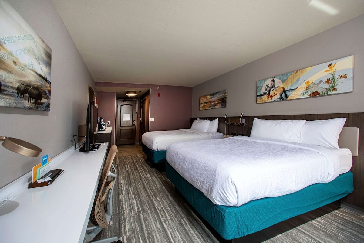 Ein Hotelzimmer mit zwei Betten, einem Schreibtisch, einem Stuhl und Bildern an den Wänden.