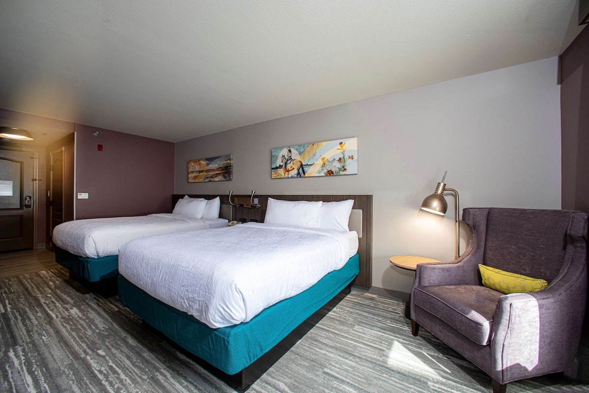 A hotel room with two beds, a chair, a small table, and artwork on the walls.