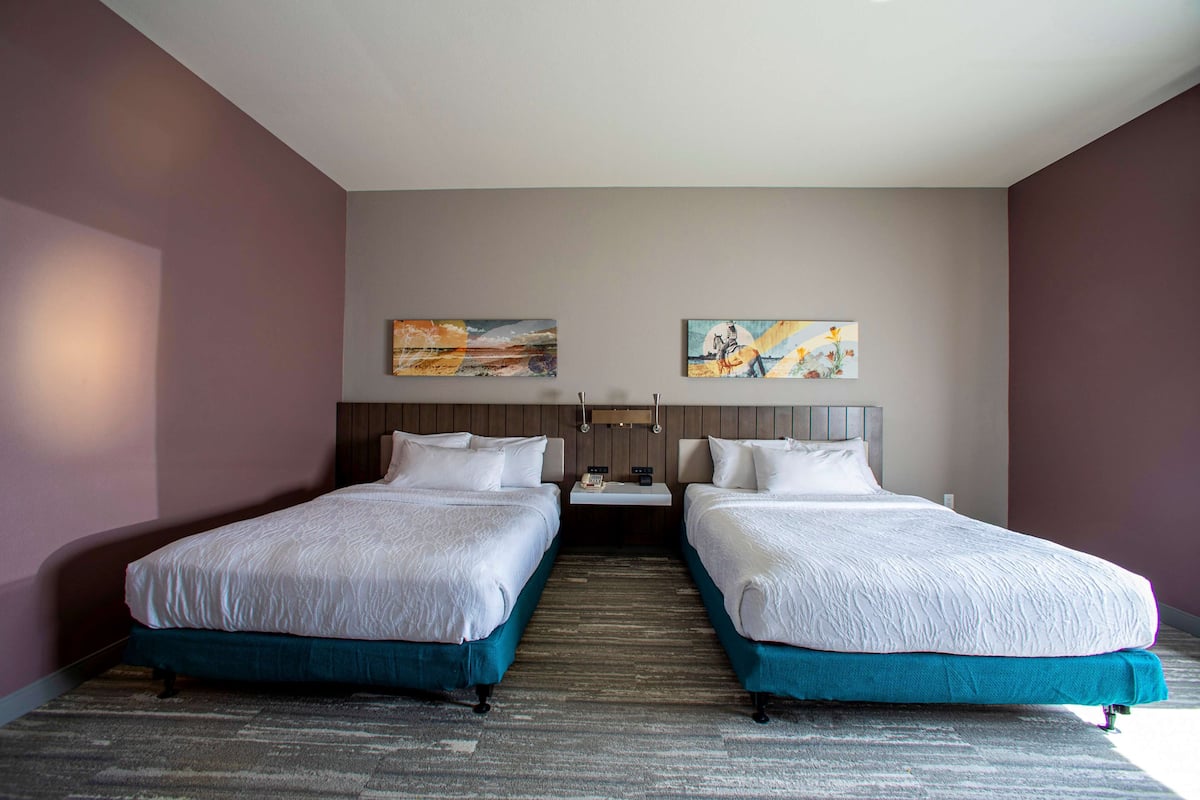 A hotel room with two beds, a nightstand, and artwork on the walls.