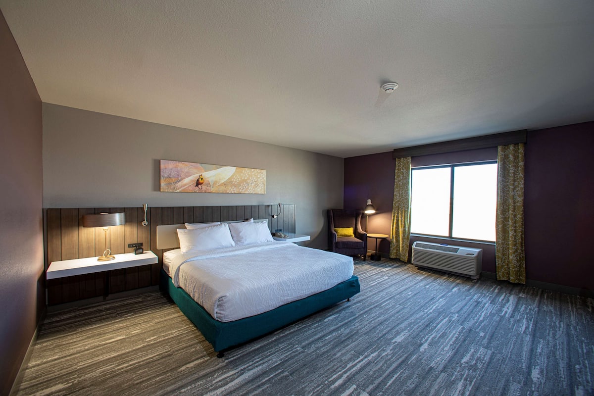 A hotel room with a large bed, bedside tables with lamps, a window with curtains, and a wall-mounted artwork.