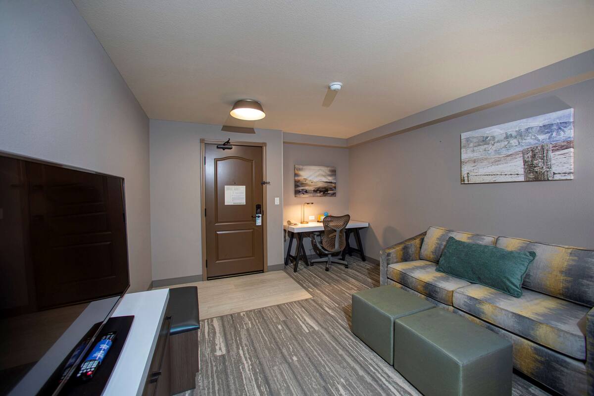 A hotel room with a flat-screen TV, a sofa, a desk with a chair, and a painting on the wall.