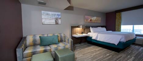 A hotel room with a sofa, a bed, a nightstand, and a window.