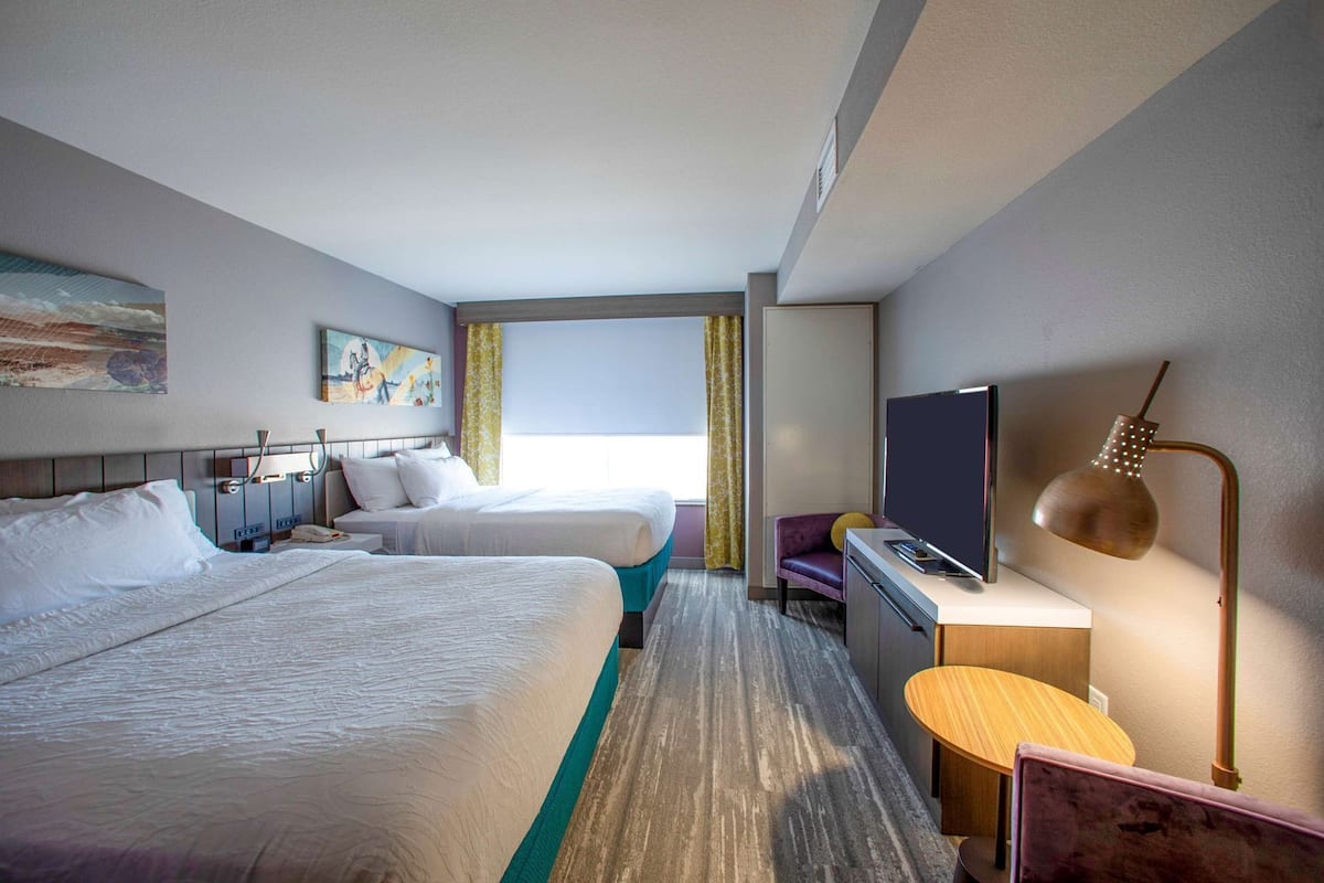 A hotel room with two beds, a desk, a television, and a lamp.