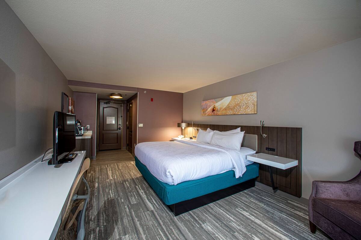 A hotel room with a bed, bedside table, TV, and a desk with a chair.