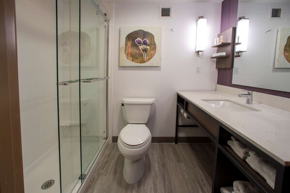Une salle de bain moderne avec une douche à parois de verre, des toilettes, un lavabo avec un miroir et un porte-serviettes fixé au mur.