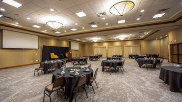 A conference room with multiple tables and chairs, a projector screen, and a stage with curtains.