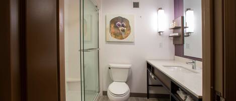 A modern bathroom with a glass shower enclosure, a toilet, a sink with a mirror, and a wall-mounted towel rack.
