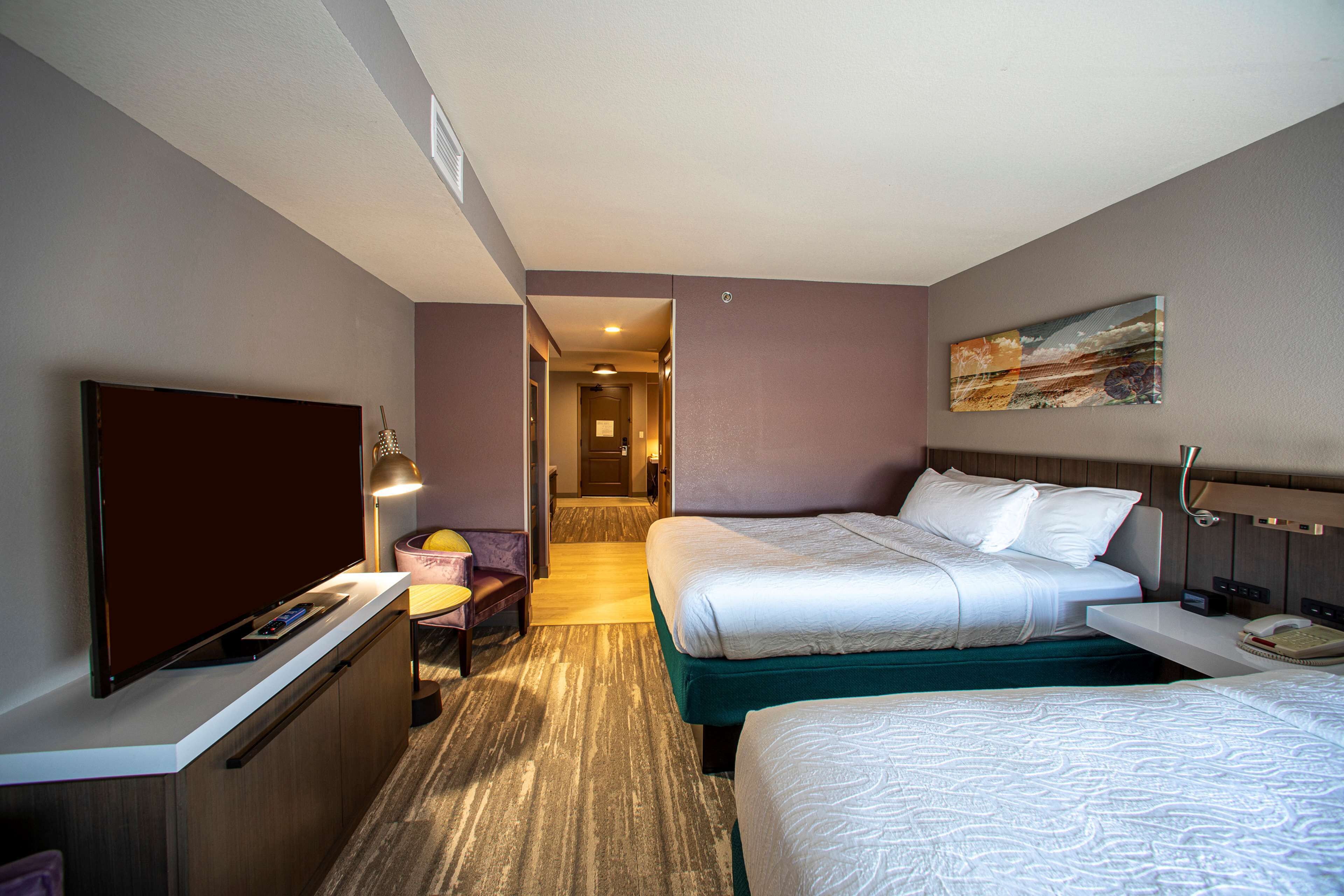 Een hotelkamer met twee bedden, een bureau, een flatscreen-televisie, een lamp en een schilderij aan de muur.