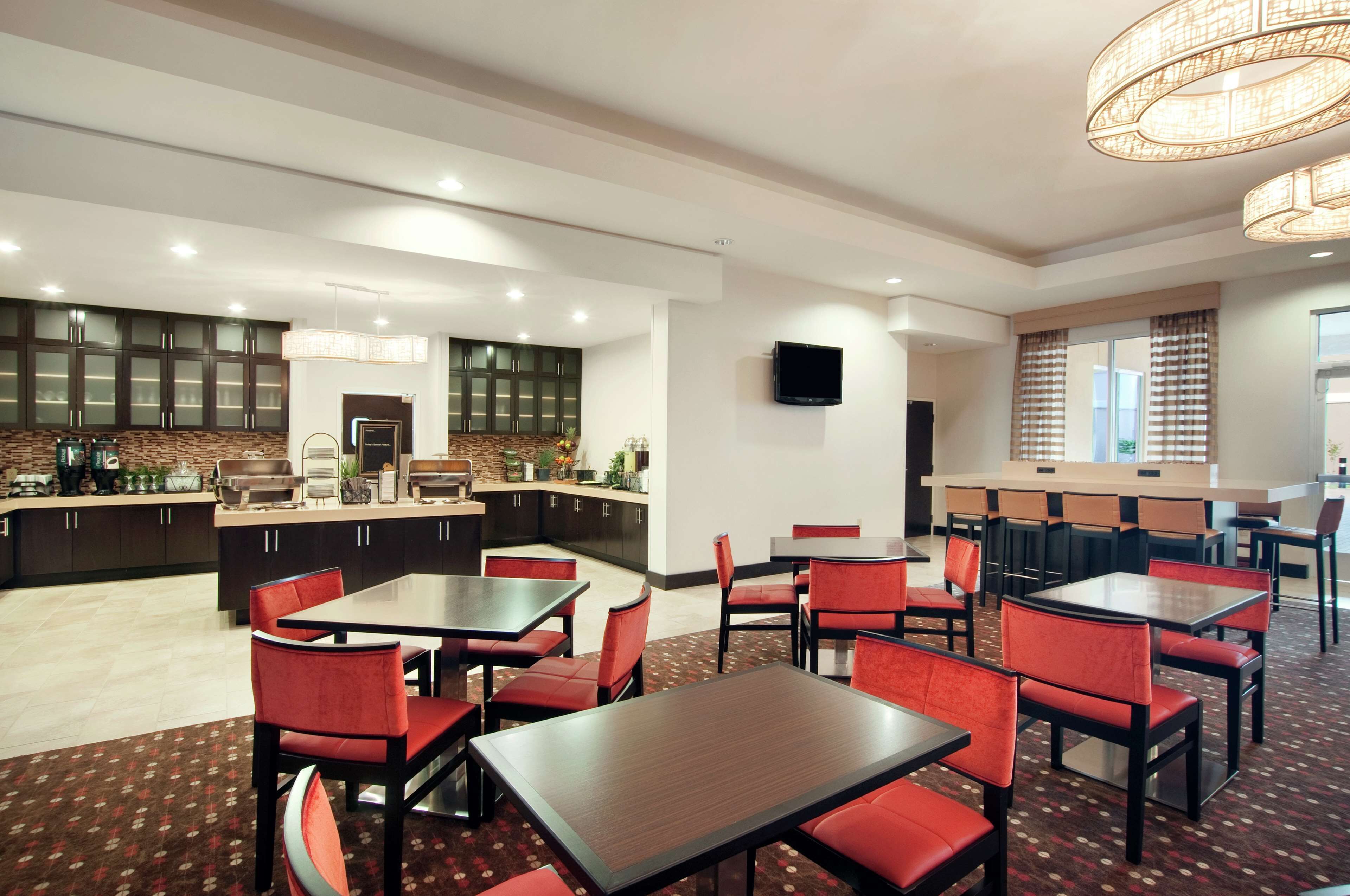 A modern restaurant with red chairs and tables, a kitchen area, and a TV on the wall.