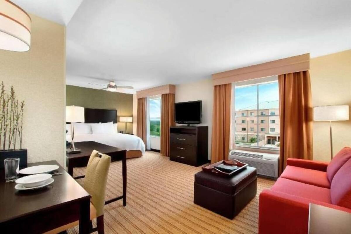 A hotel room with a bed, a TV, a desk with a chair, a red sofa, and a window with curtains.