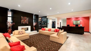 Un salón moderno con sofás color beige, cojines rojos, un tapiz estampado y una chimenea.