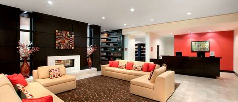 A modern living room with beige sofas, red cushions, a patterned rug, and a fireplace.