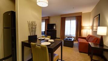 Une chambre d’hôtel équipée d’une table à manger pour quatre personnes, d’un canapé, d’une télévision et d’un réfrigérateur.