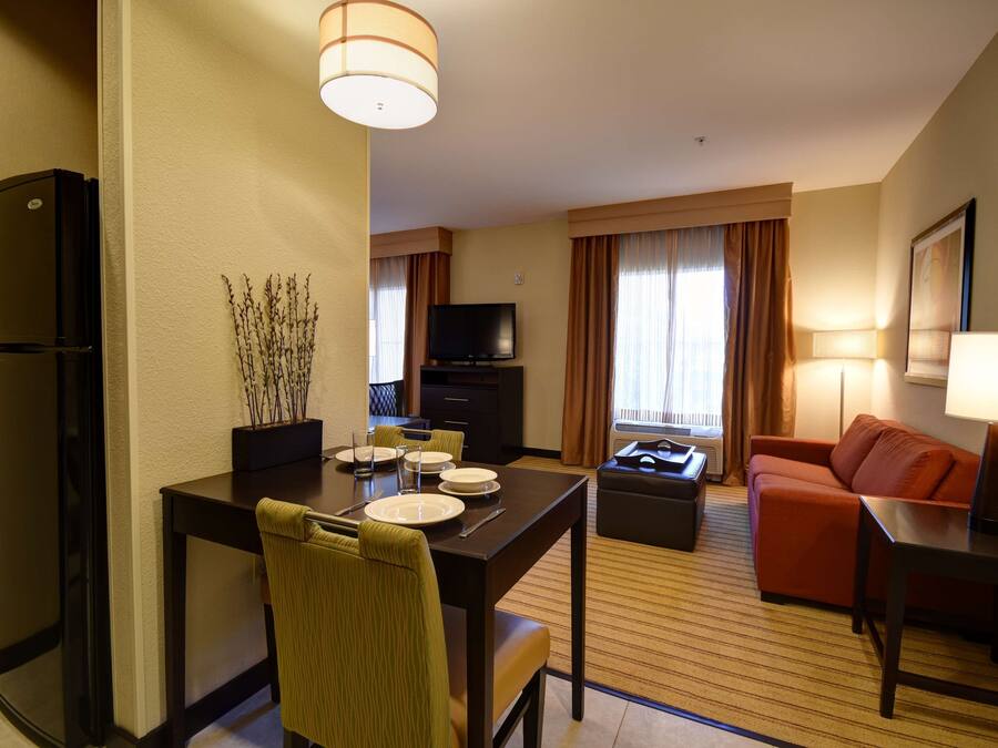 A hotel room with a dining table set for four, a sofa, a TV, and a refrigerator.