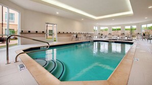 Una amplia piscina interior con un trampolín de un metro, rodeada de sillones de descanso y suelo de baldosas.
