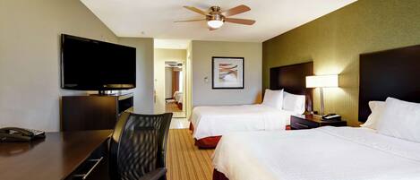 A hotel room with two beds, a desk with a chair, a television, and a ceiling fan.