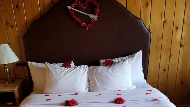 A hotel room with a wooden headboard, a bed with white linens, and a heart-shaped decoration on the headboard.
