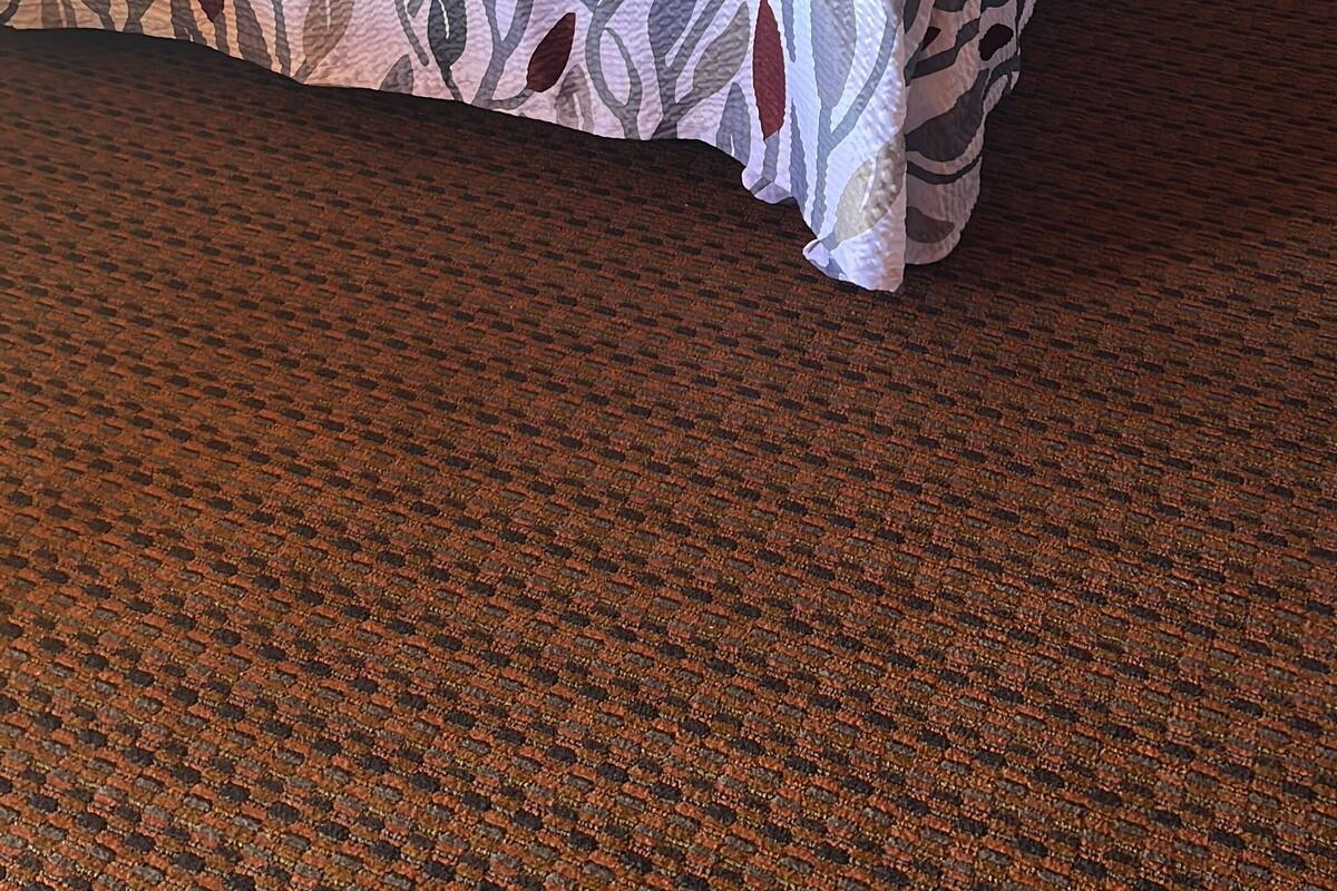 Ein Bett mit einem gemusterten Überwurf, einem Holzkopfstück und einem Teppichboden.