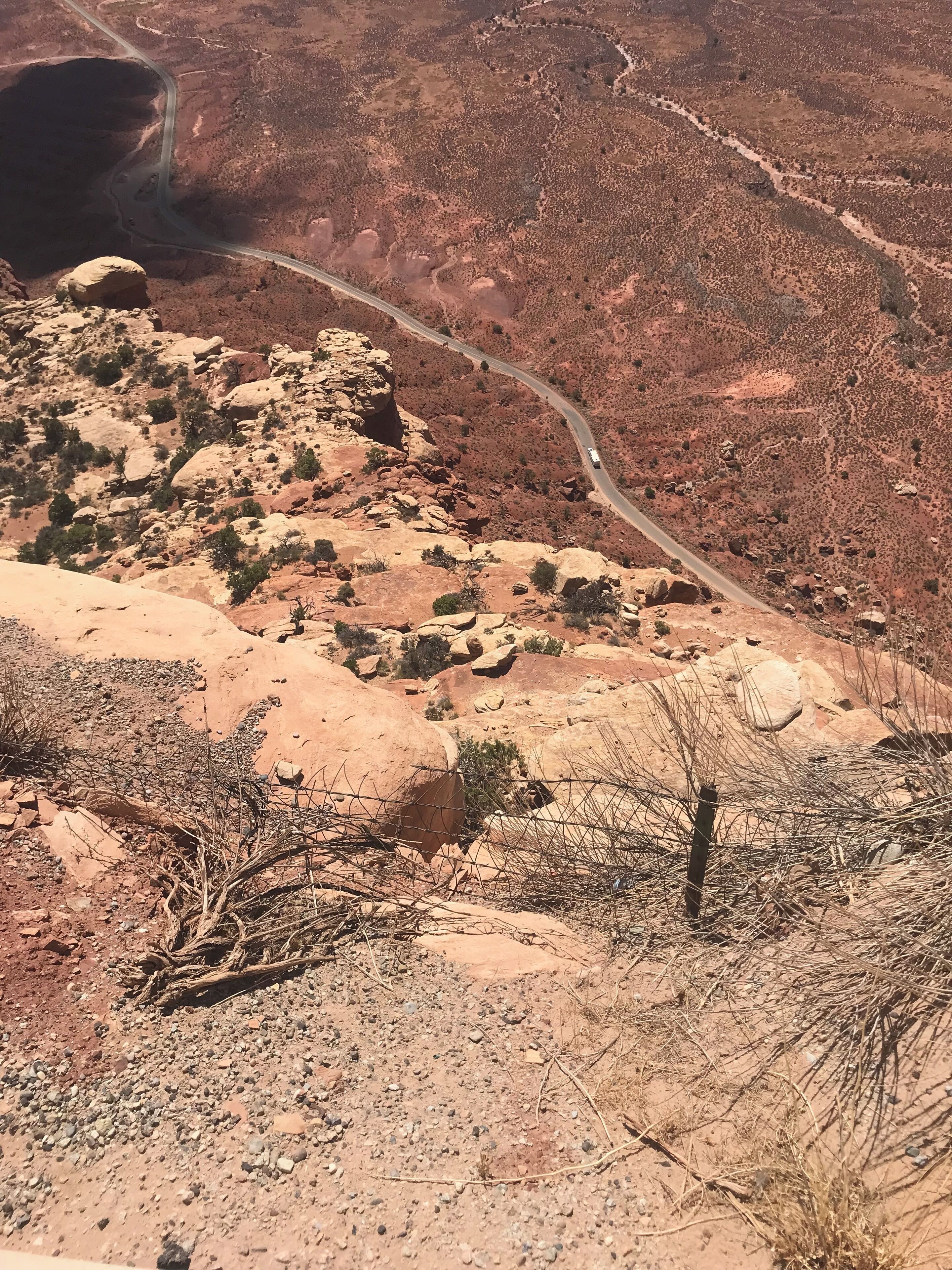 A rugged landscape with a winding road, rocky terrain, sparse vegetation, and a clear sky.