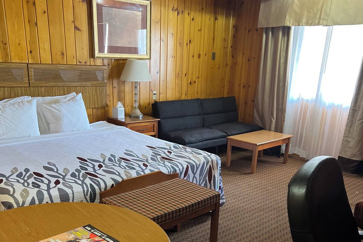 Ein Hotelzimmer mit einem Bett, einem Schlafsofa, einem kleinen Tisch, einem Sessel und einem an der Wand befestigten Fernseher.