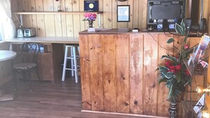 A wooden interior with a bar area, a television, and a small seating area with a chair and a stool.