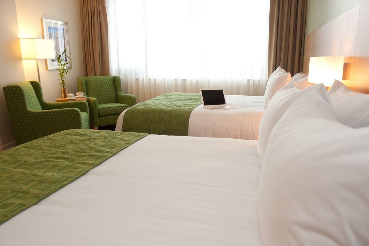 A hotel room with two beds, a desk, a laptop, a lamp, and a plant.