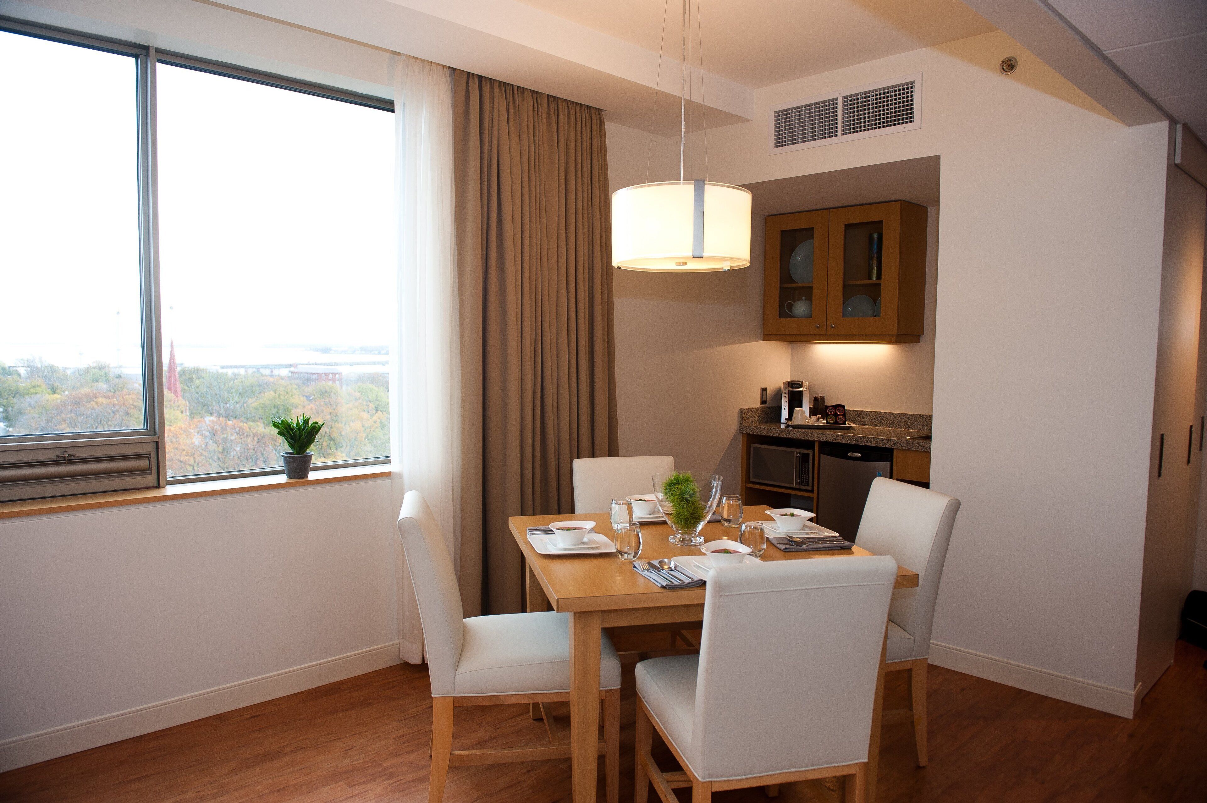 A dining area with a table set for four, a window with curtains, and a view of the outdoors.