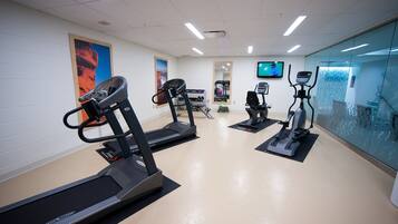 A fitness center with treadmills, elliptical machines, and a television screen.