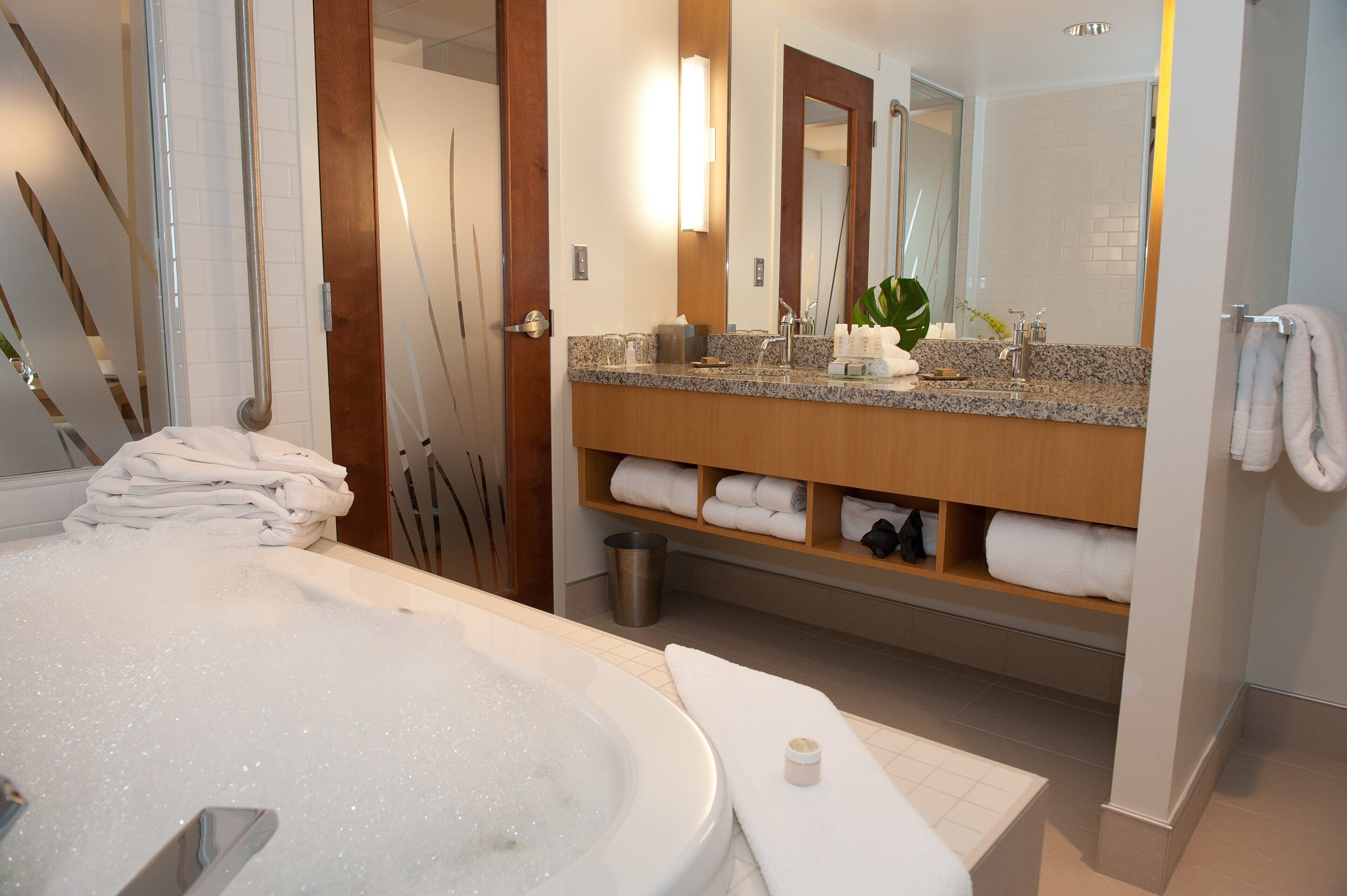 A modern bathroom with a large bathtub, a wooden vanity with a mirror, and neatly folded towels.