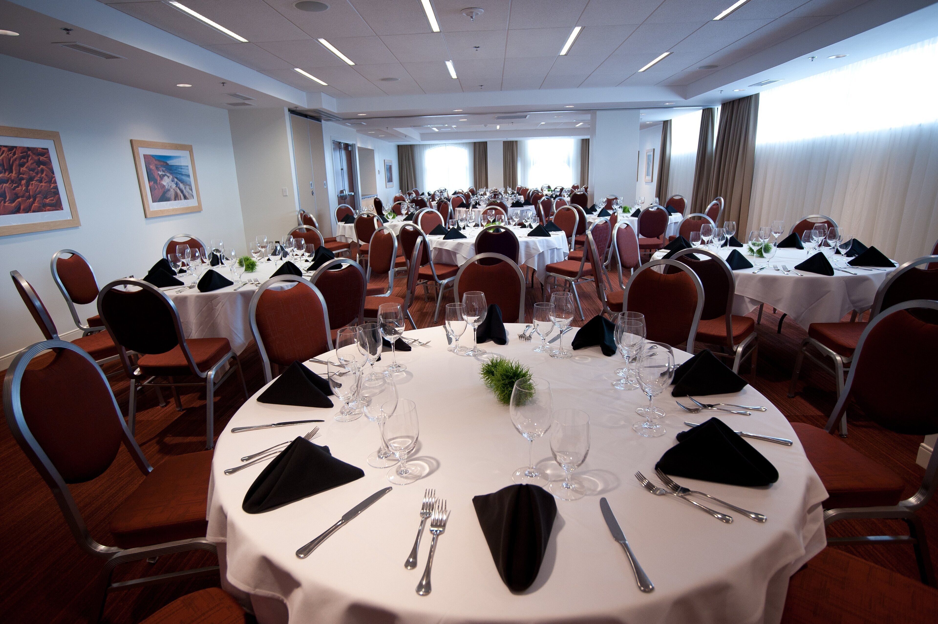 A conference room with multiple round tables, each set with white tablecloths, silverware, and glassware.