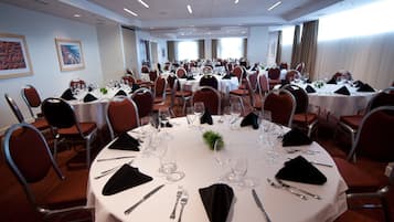 A conference room with multiple round tables, each set with white tablecloths, silverware, and glassware.
