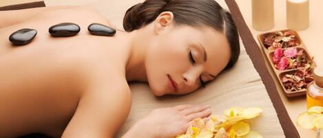A person receiving a back massage with stones and flowers on a massage table.