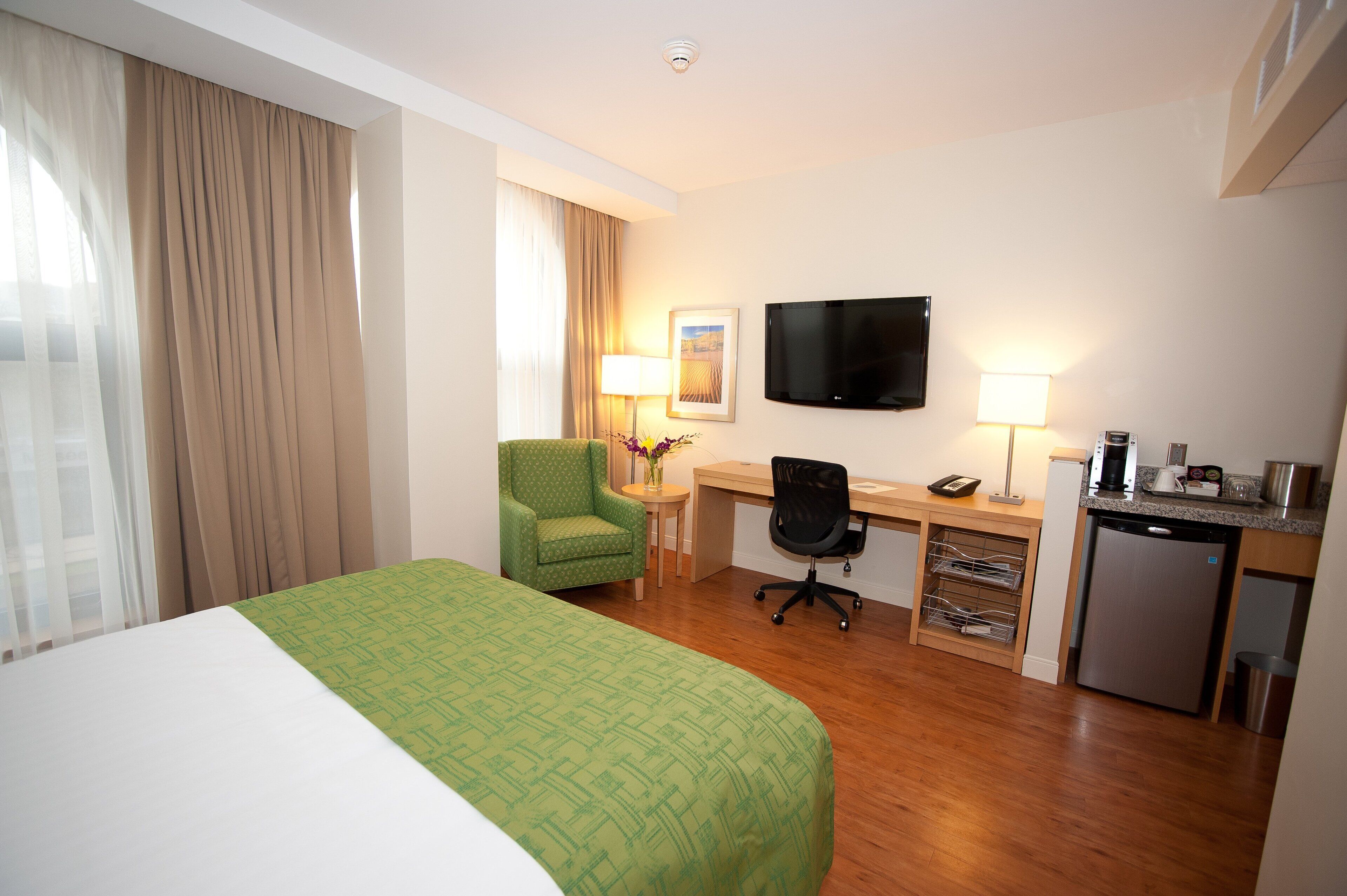 Une chambre d’hôtel équipée d’un lit, d’un bureau, d’une chaise, d’une télévision, d’une lampe et d’une petite kitchenette.