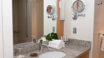 A bathroom with a granite countertop sink, two wall-mounted mirrors, a handheld mirror, and a towel rack.