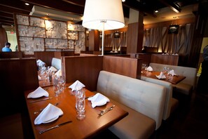 A restaurant with wooden booths, tables set with white napkins, silverware, and wine glasses.