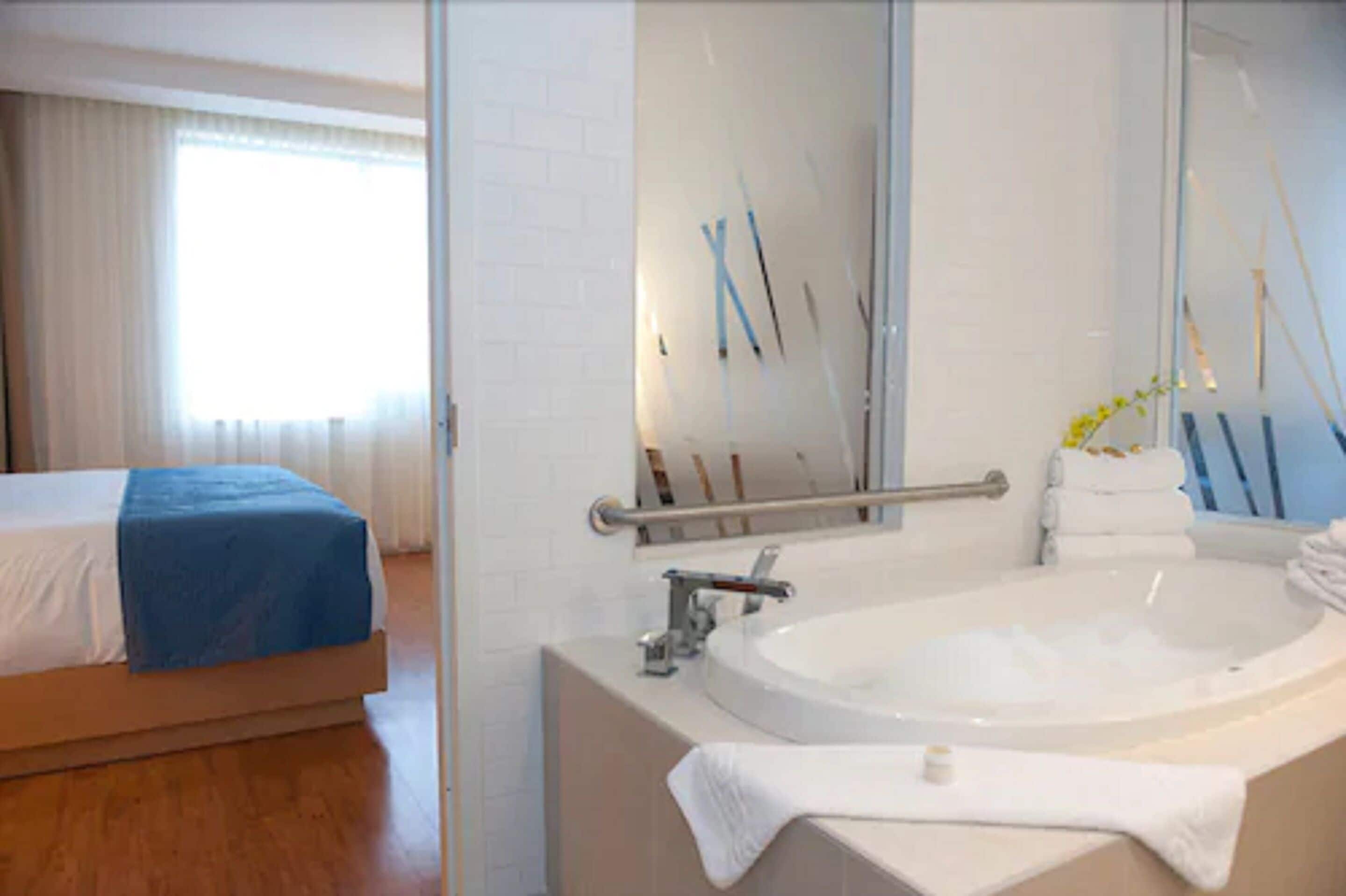 Une chambre d’hôtel avec un lit, une grande salle de bain dotée d’une baignoire et un miroir.