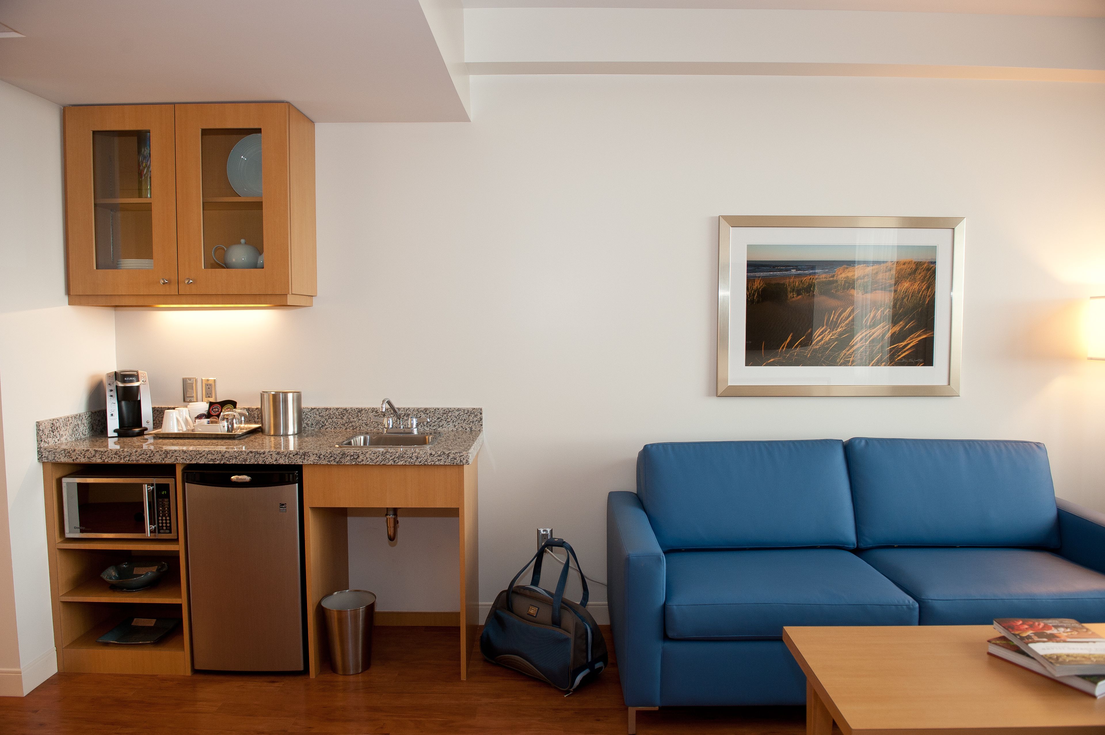 A compact living space with a kitchenette, a blue sofa, and a framed picture on the wall.