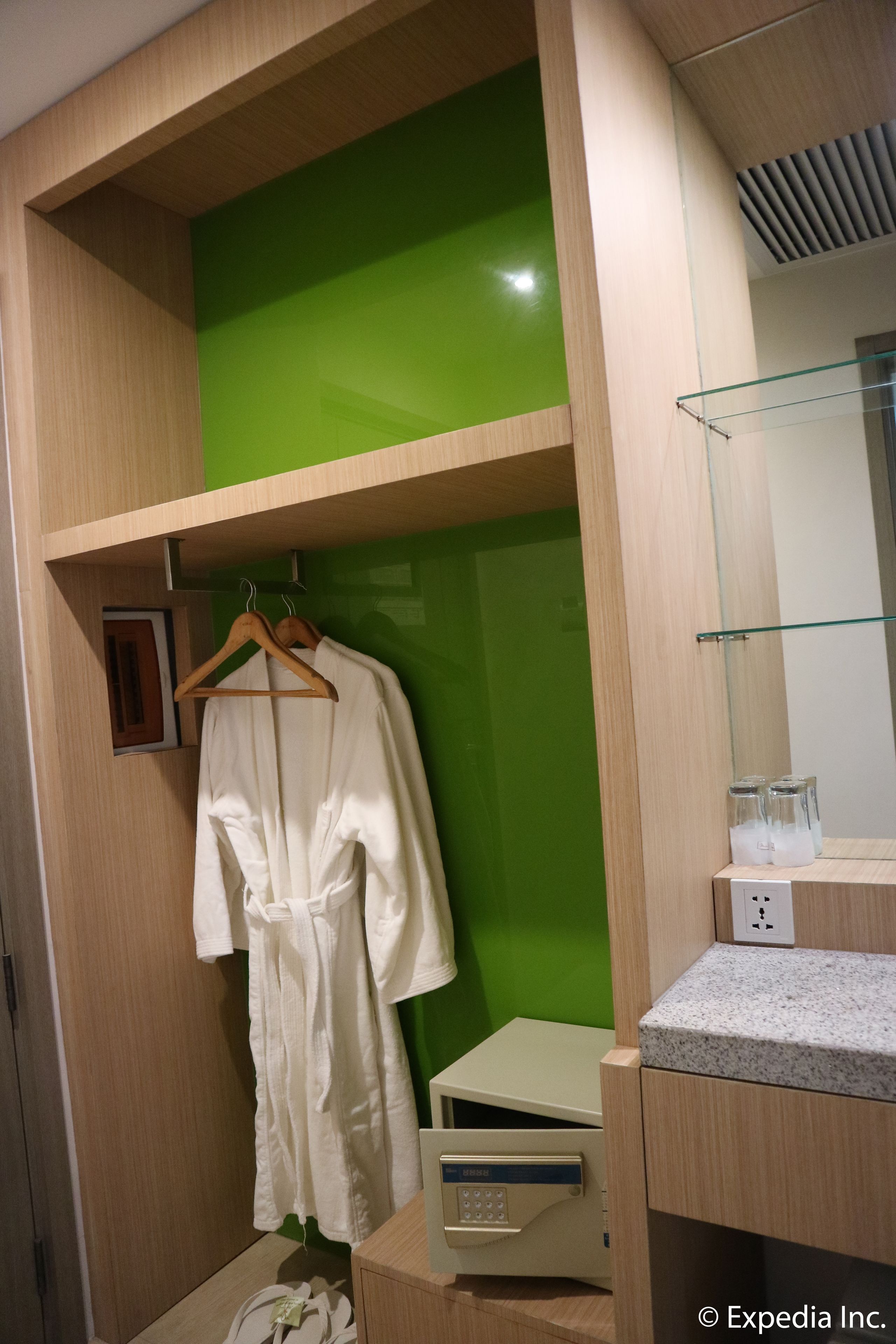 A wooden wardrobe with a green panel, a white robe hanging, and a small table with a control panel.