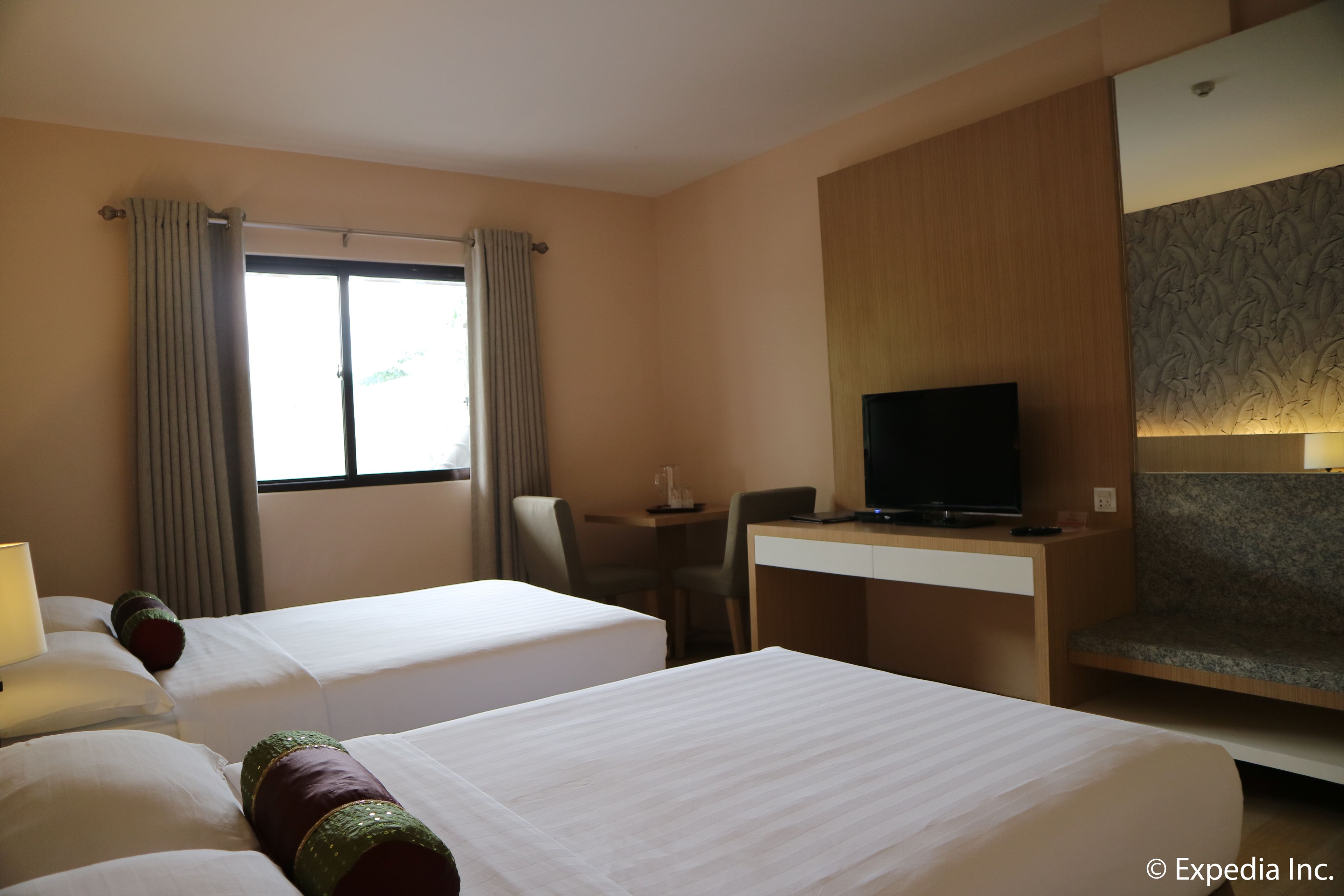 A hotel room with two beds, a desk with a television, and a window with curtains.
