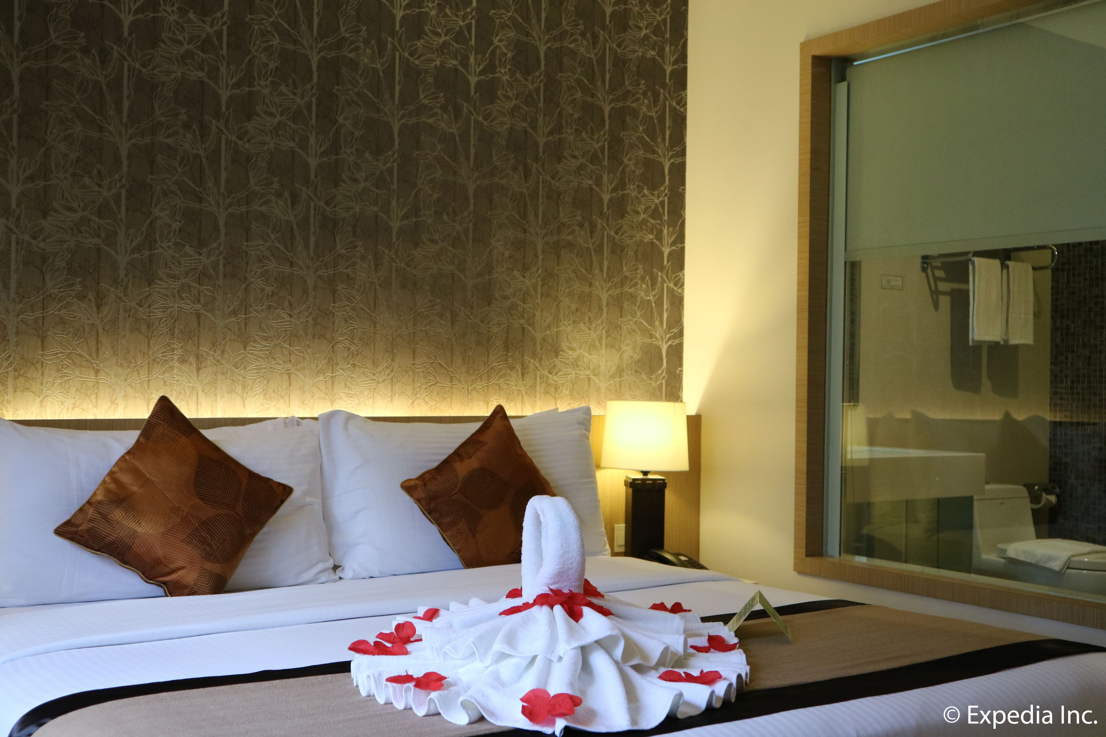 A hotel room with a neatly made bed, a large mirror, and a patterned wallpaper.