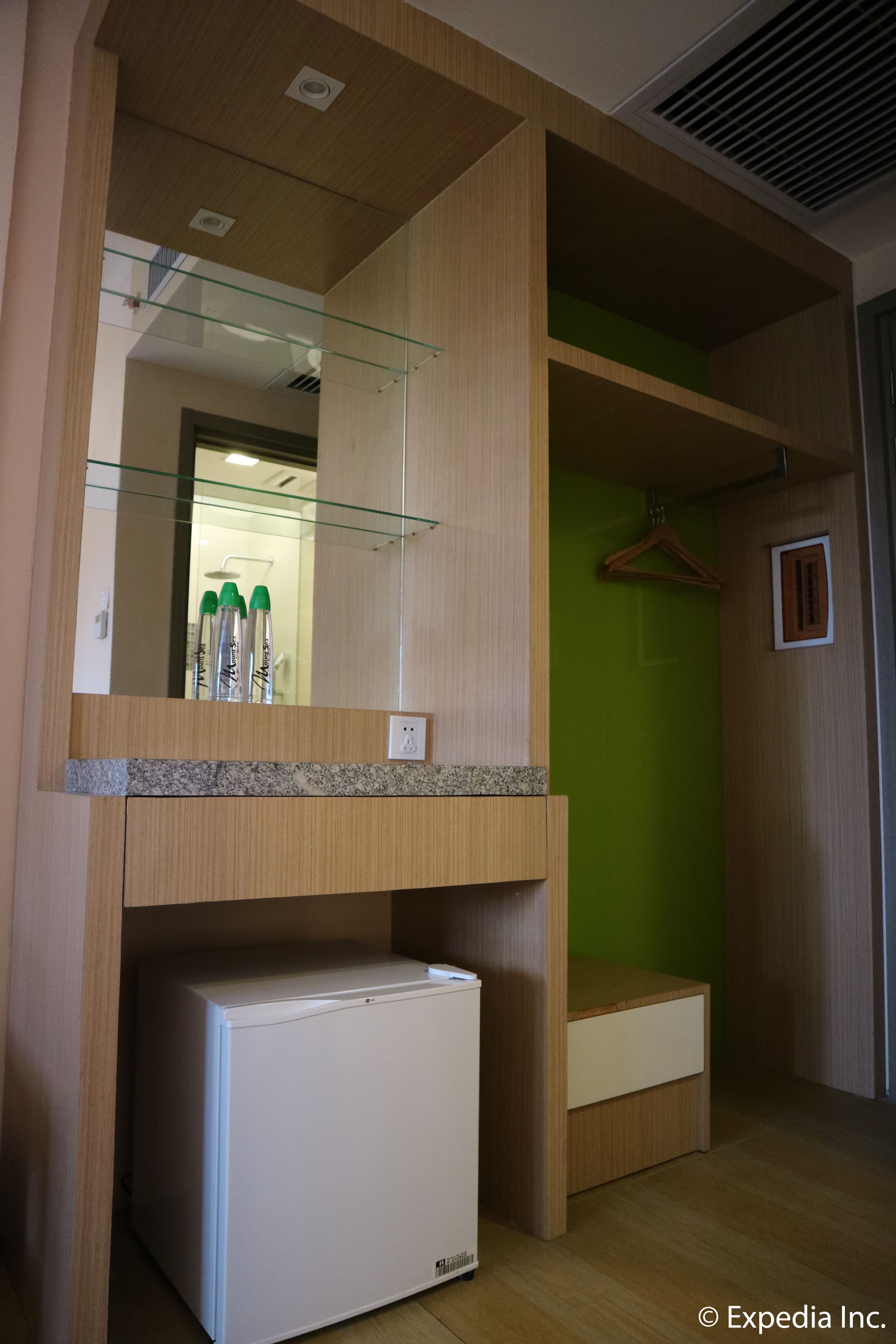 A compact room with a built-in refrigerator, a mirror, and a hanging coat rack.