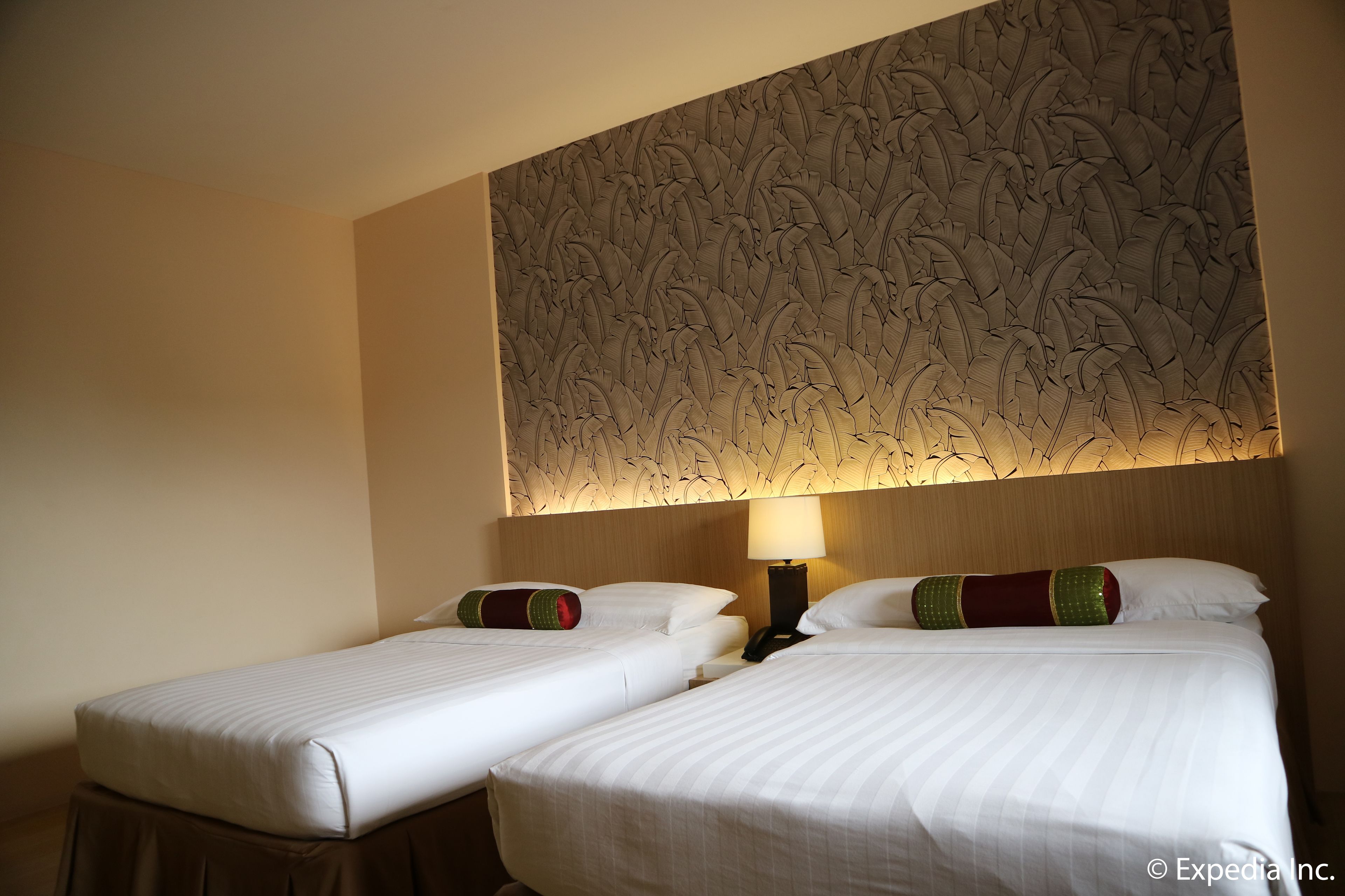 A hotel room with two single beds, a decorative wall panel, a nightstand with a lamp, and a telephone.