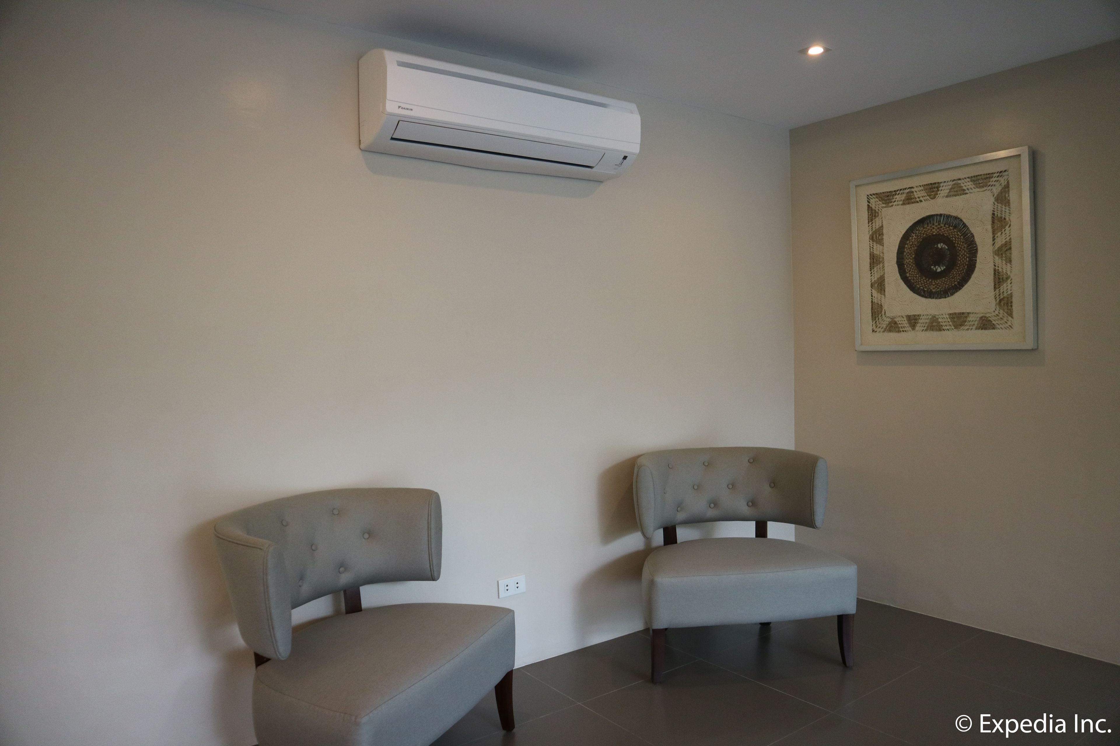 A room with two grey upholstered chairs, a white air conditioning unit, and a framed artwork on the wall.