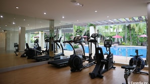 A gym with various exercise equipment, a large mirror, and a view of a swimming pool.