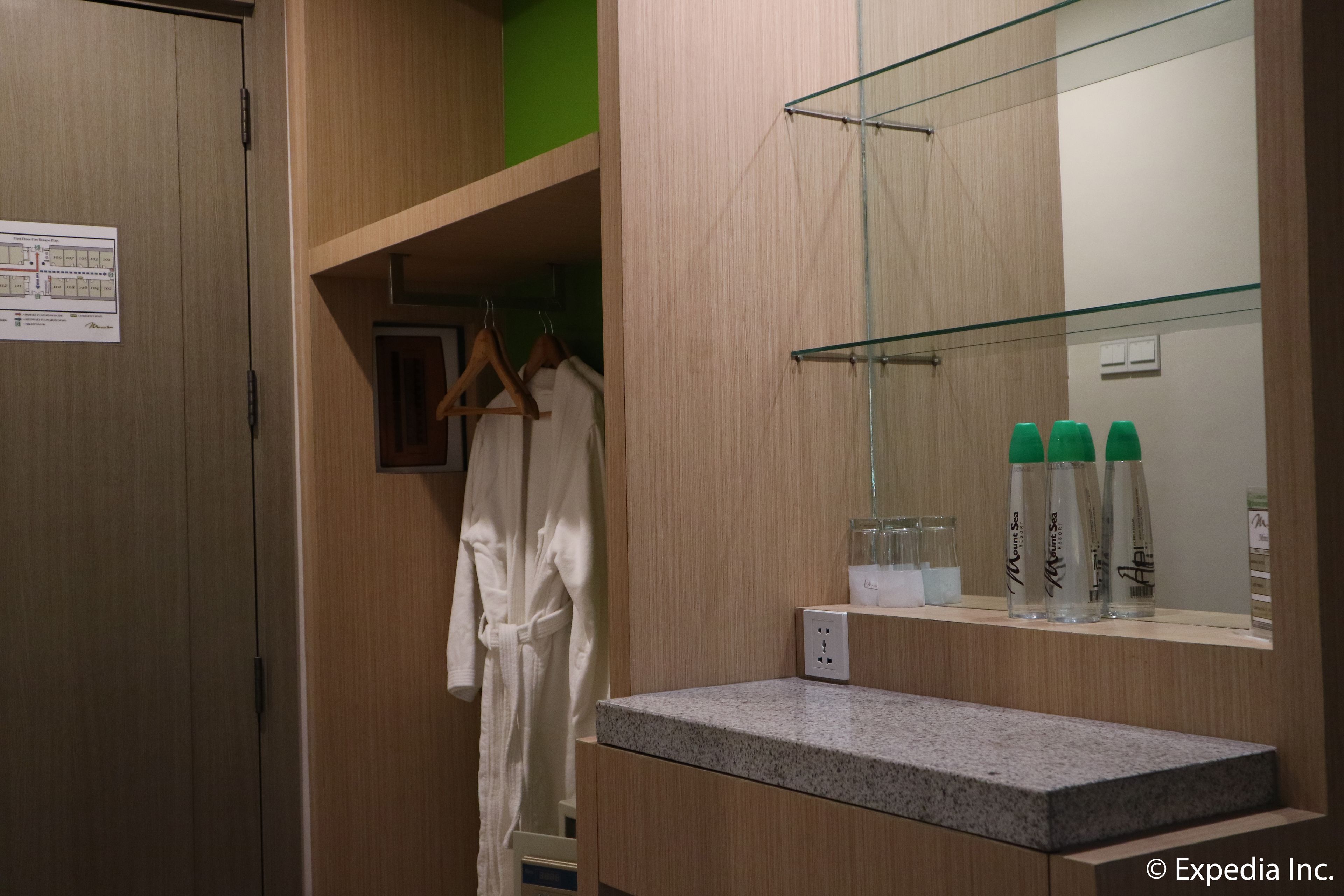A hotel bathroom with a wooden vanity, a robe hanging on a rack, and a mirror with toiletries.