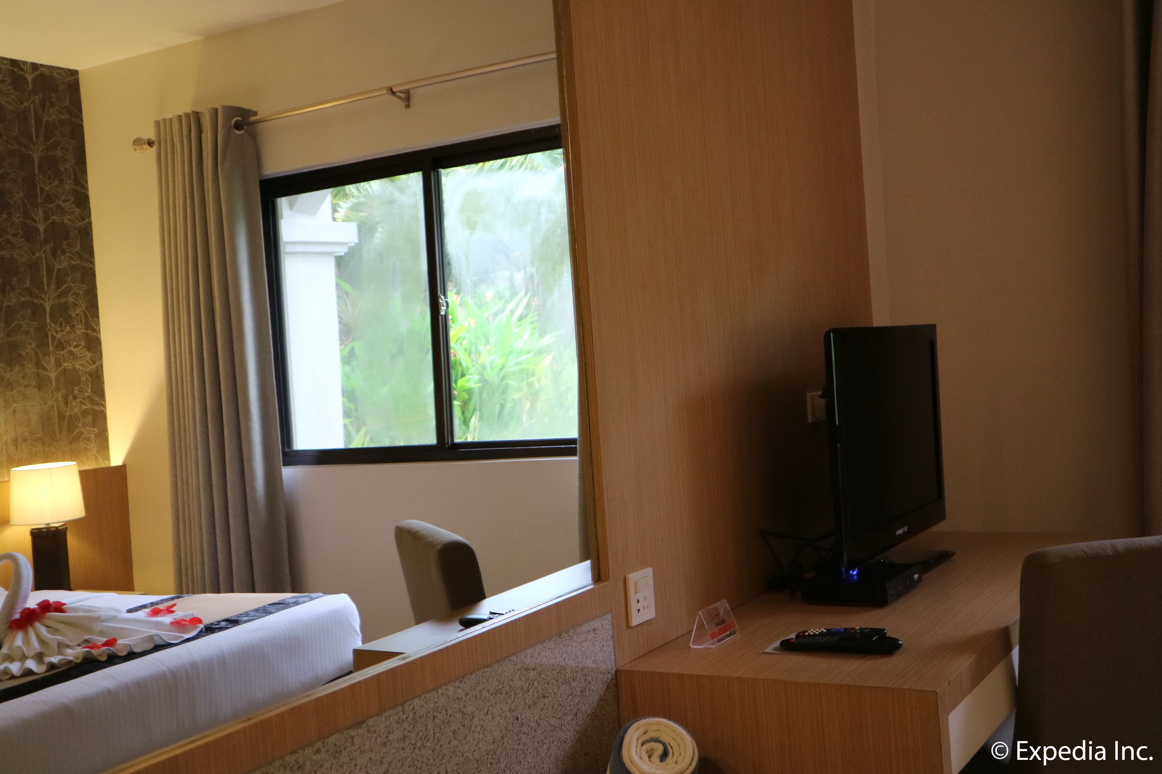 A hotel room with a bed, a desk with a television, a chair, a lamp, and a window with curtains.