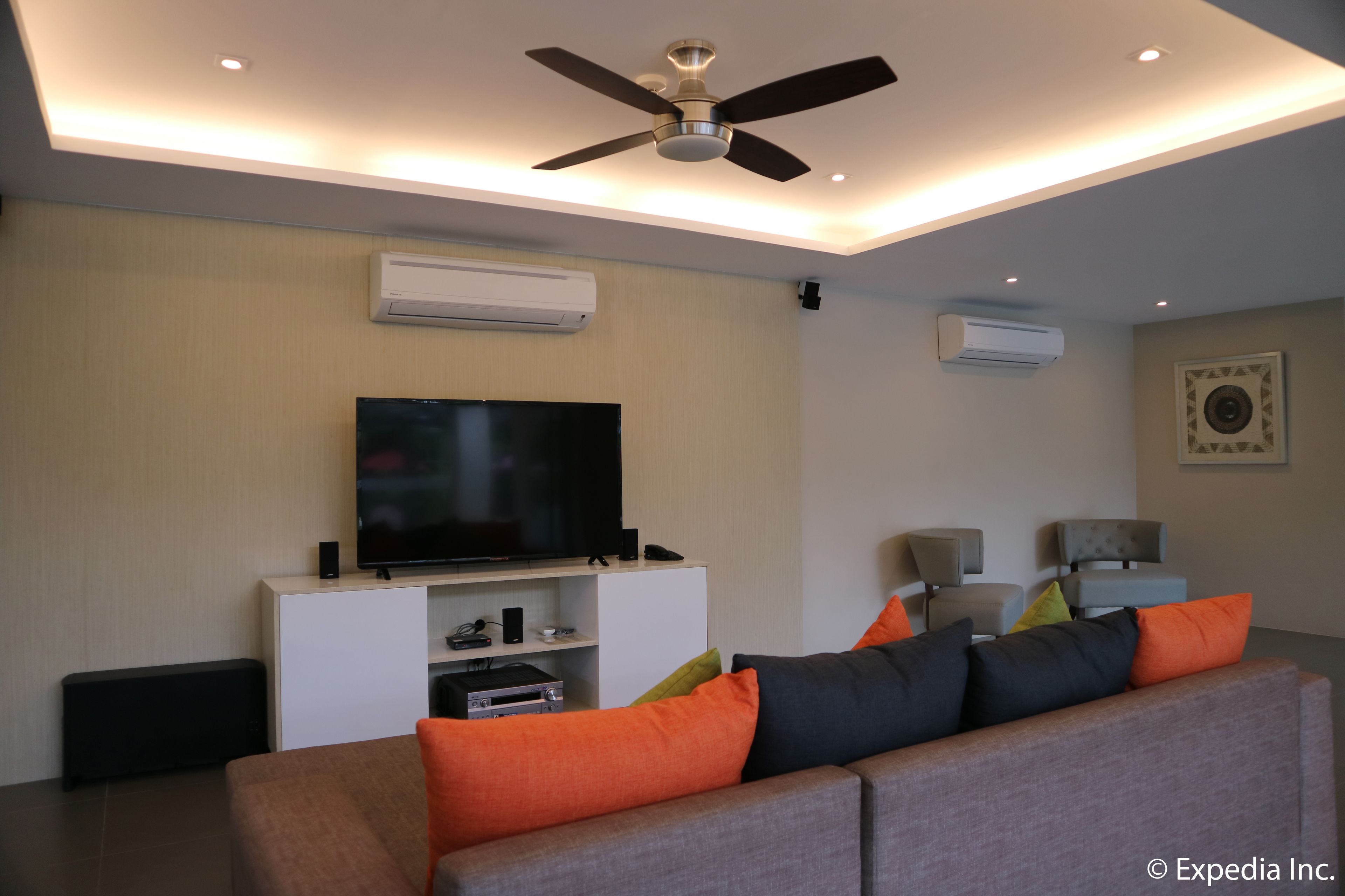 A modern living room with a flat-screen TV, ceiling fan, and air conditioning units.