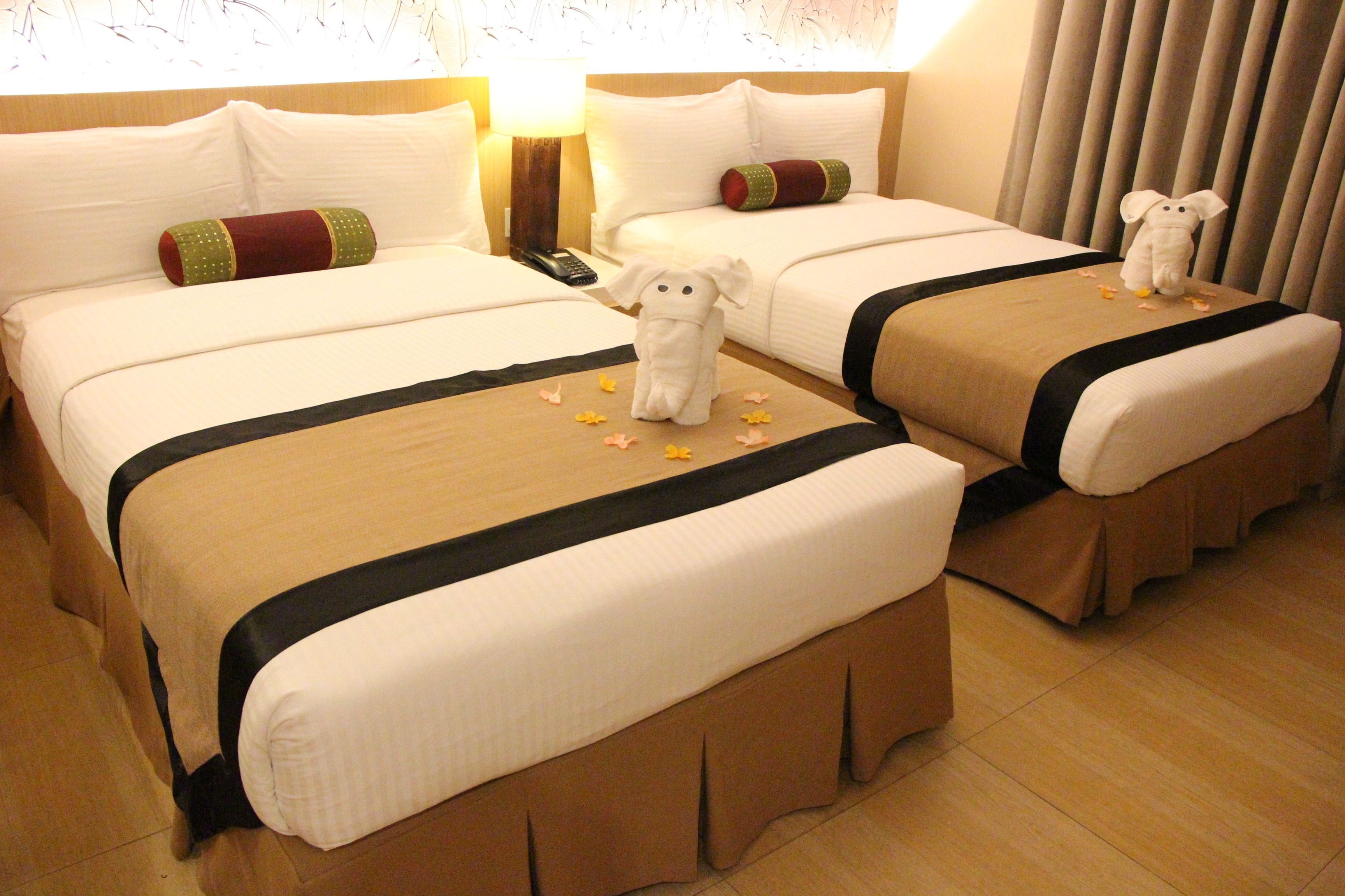 A hotel room with two beds, each with a plush toy and a remote control on the nightstand.