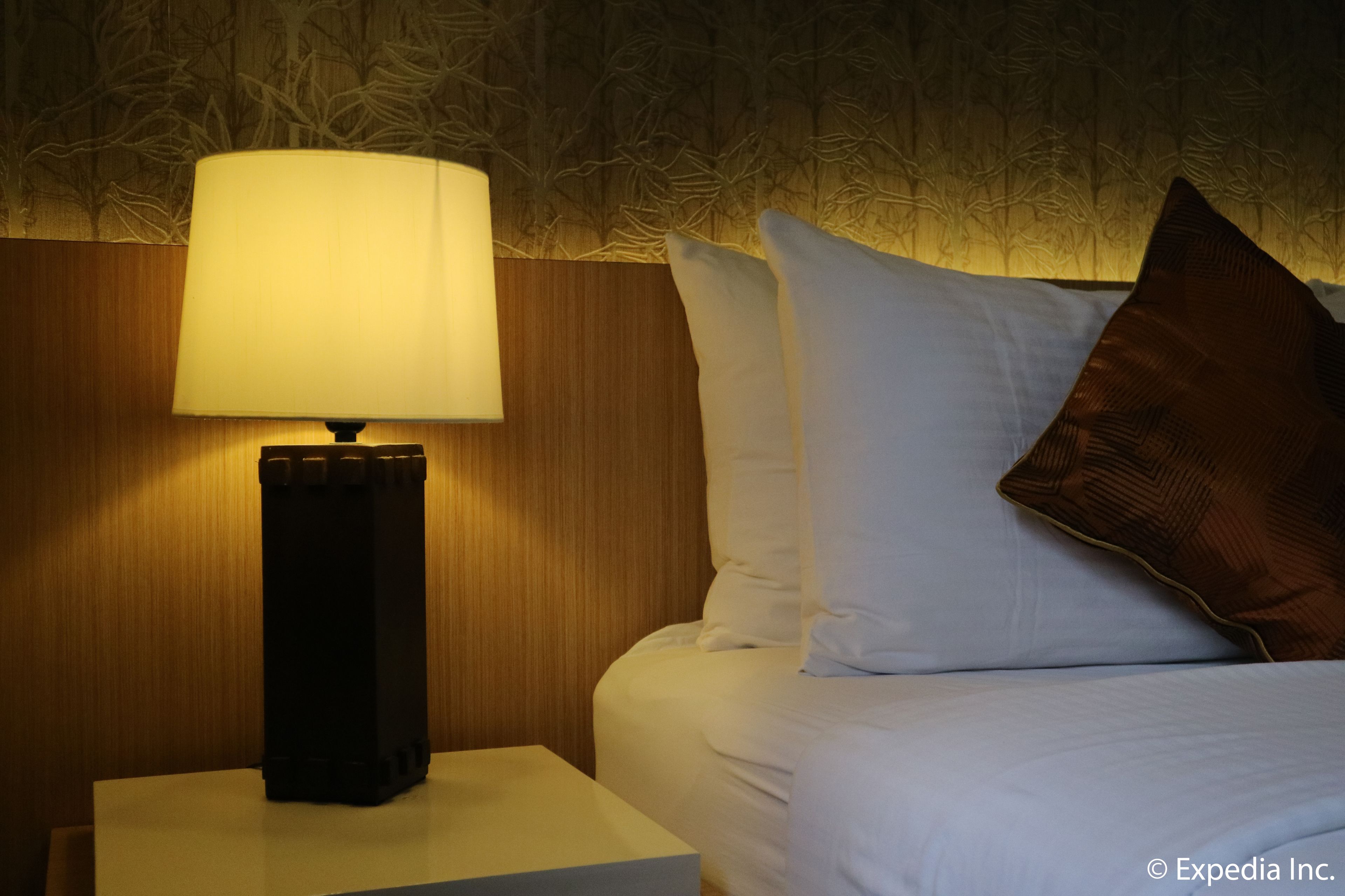 A neatly made bed with white and brown pillows, a bedside lamp, and a wooden headboard.