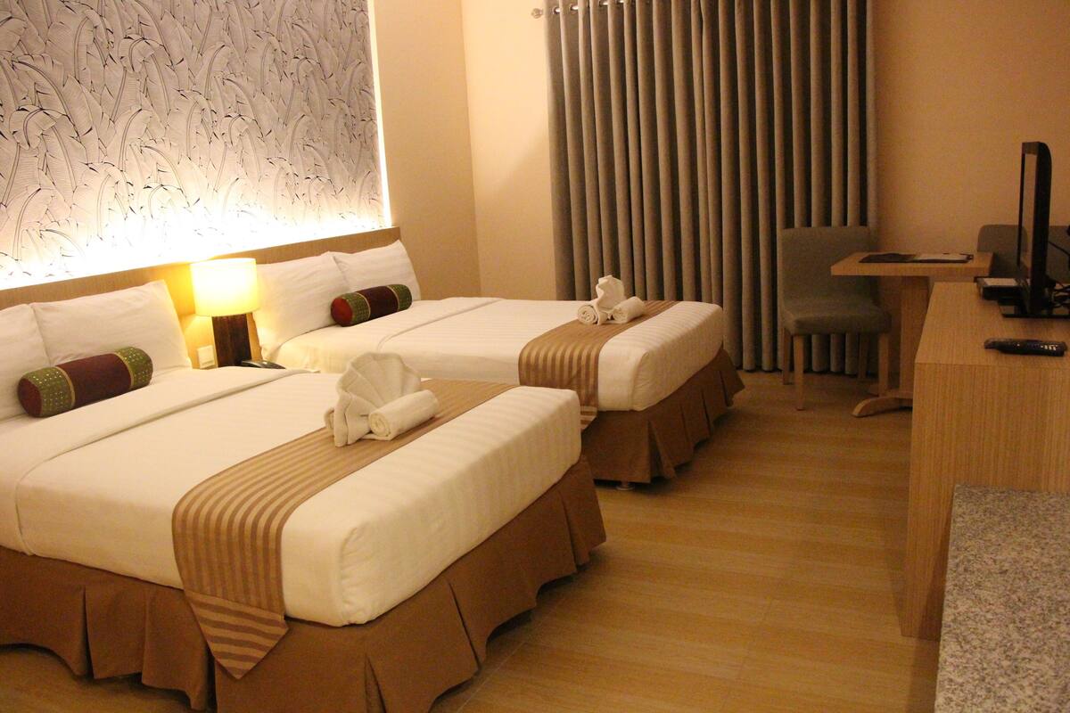 A hotel room with two beds, a desk, a chair, and a television.